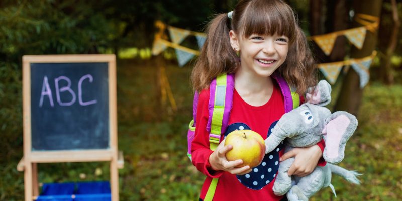 Cheerful schoolgirl with a backpack and an apple. Back to school. The concept of education, school, childhood, study.